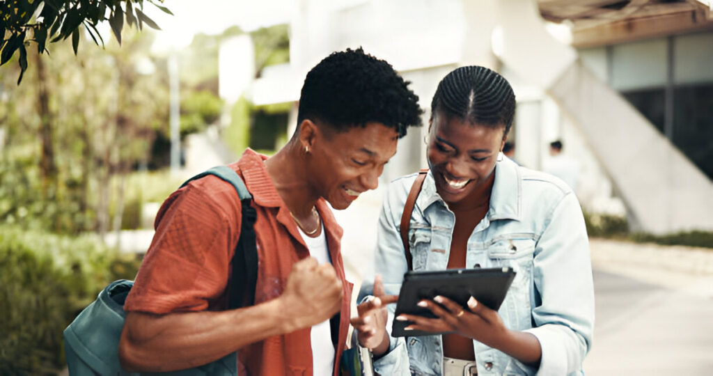 Student happily applying online for the Too Cool to Pay for School Scholarship on a laptop.