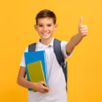 how to create a scholarship fund: a smiling student holding books and giving a thumbs up.