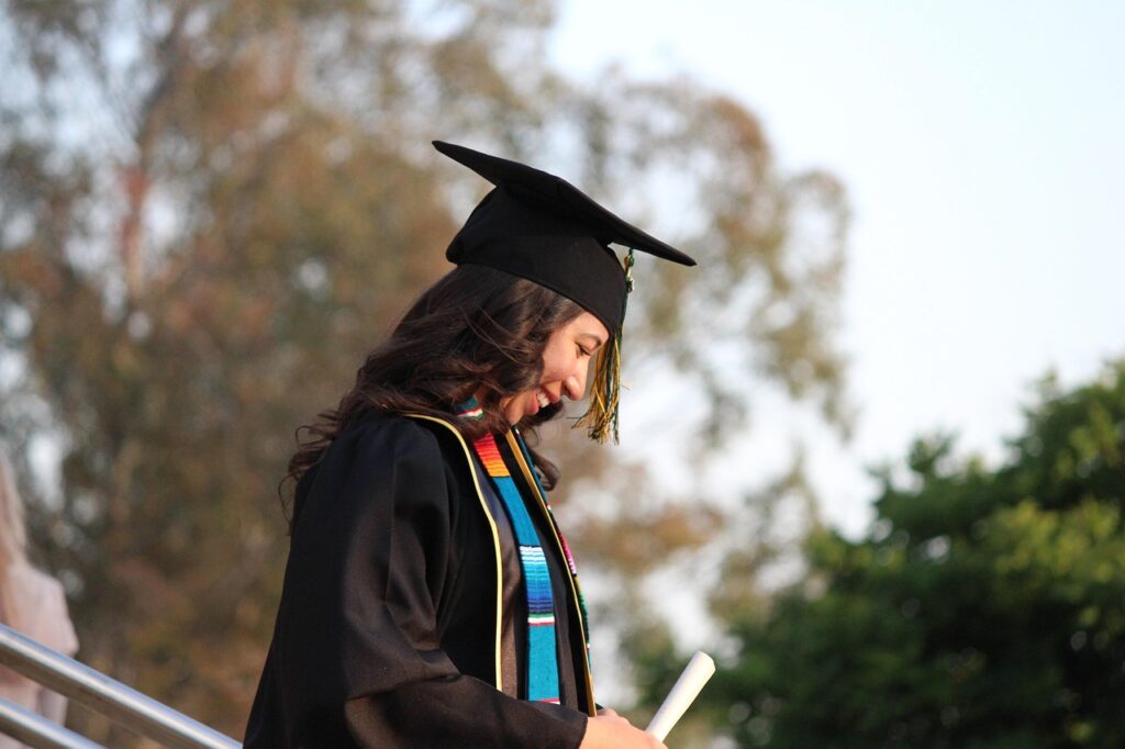 Young female student graduate in cap and gown, smiling proudly while holding her diploma, embodying the academic success and future leadership potential supported by the GE Reagan Scholarship.